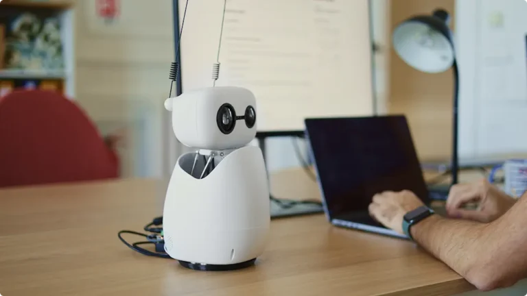 Le mini-robot Reachy Mini de Hugging Face à côté d'un ordinateur portable sur une table.
